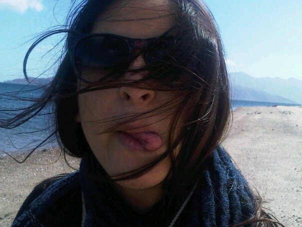 foto del rostro de una mujer al aire libre, usando lentes de sol y sacando la lengua